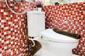 A bathroom with a white toilet, a shower, and a tiled wall. - Vibrant Look 2Br At Apartment Green Pramuka City (Jakarta)