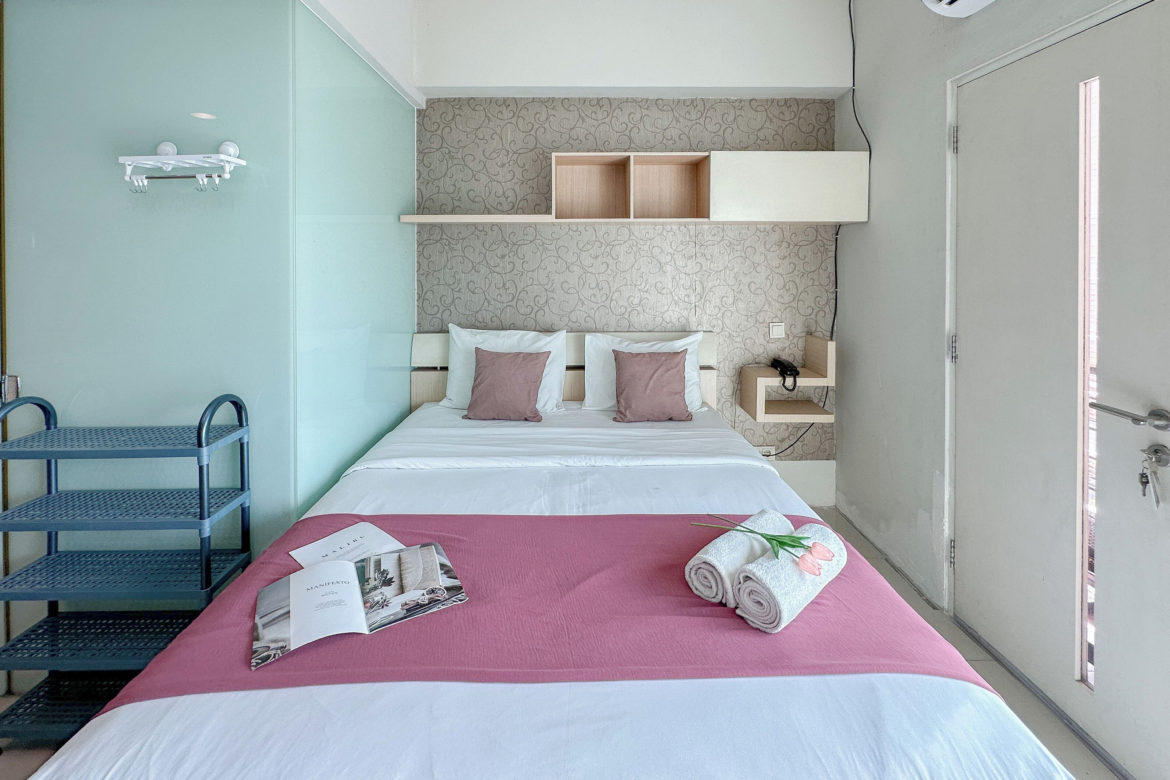 A neatly arranged hotel room with a bed, a desk, and a shelf with toiletries.