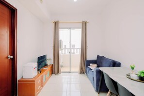 A modern living room with a sofa, a coffee machine, a TV, and a balcony with curtains. - Strategic 1Br Apartment At Marina Ancol (Jakarta)