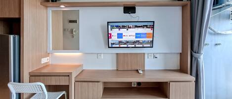 A modern room with a wooden desk, a white chair, a mounted TV displaying various apps, and a small plant on the desk.