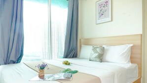 A neatly made bed with white linens, a small vase with flowers, and a magazine on the bed. - Homey White 2Br At Grand Kamala Lagoon Apartment (Bekasi)