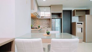 A modern kitchen with a glass dining table, white chairs, and a built-in oven. - Wood Accents 2Br At Tamansari The Hive Apartment (Jakarta)