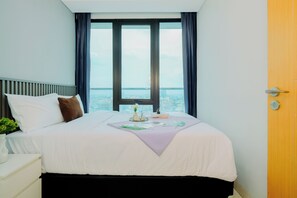 A hotel room with a large bed, a bedside table with a vase, and a view of the city through a window. - Spacious Grey 2Br At Capitol Suites Apartment (Jakarta)