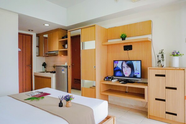 A hotel room with a bed, a TV, wooden cabinets, a small kitchenette, and a bathroom. - Contemporary And Cozy Studio Apartment Margonda Residence 3 (Depok)