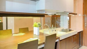 A modern kitchen with a wooden dining table, a built-in stove, and a large window. - Lovely And Cozy Studio Room At Apartment Signature Park Grande (Jakarta)