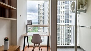 A modern apartment with a large window, a desk, and a chair, offering a view of high-rise buildings. - Enjoyable Living Studio At Apartment Pacific Garden - Campus Town @Alam Sutera (Tangerang)
