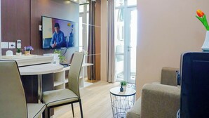 A modern hotel room with a dining area, a TV, a small round table with a plant, and a view of the outdoors. - Comfy And Homely Space 2Br At Apartment Vasanta Innopark (Cikarang)