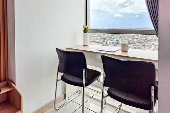 Ein modernes Zimmer mit zwei schwarzen Stühlen, einem kleinen Tisch, einer weißen Vase mit Blumen und einem Fenster mit Blick auf eine Stadtlandschaft.