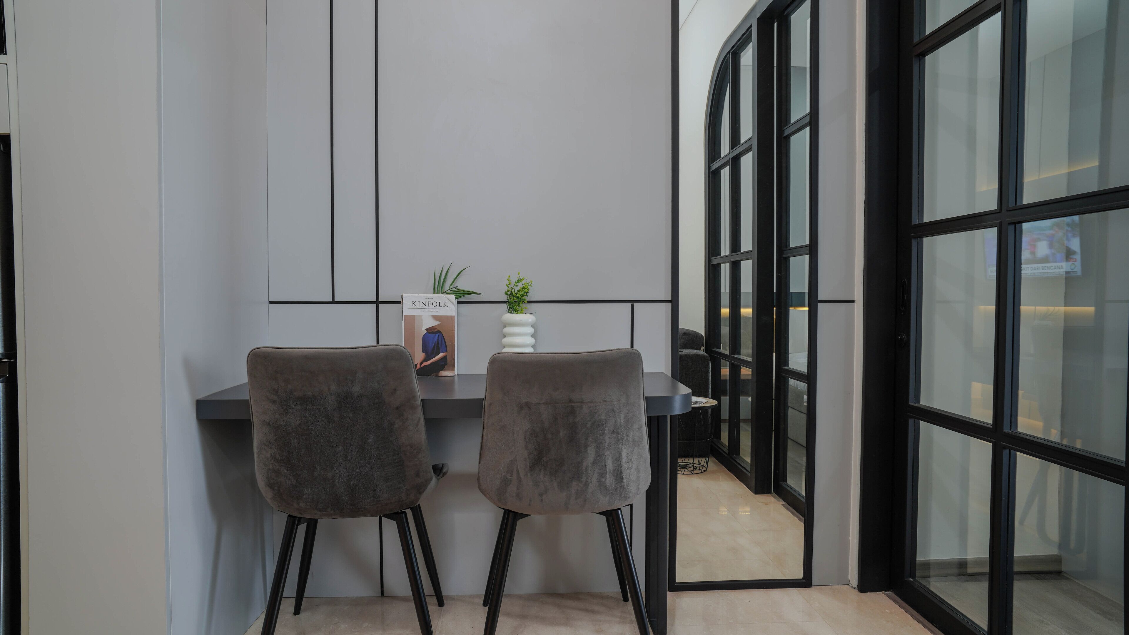Een moderne kantoorruimte met twee grijze stoelen, een witte vaas met een plant en een tijdschrift aan de muur.
