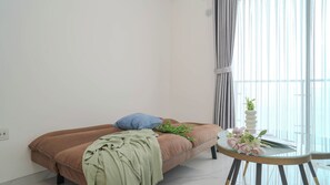 Un dormitorio moderno con un sofá marrón, una manta verde, una almohada azul y una mesa de vidrio con un jarrón de flores.