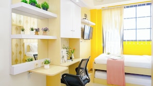 Une chambre d’hôtel avec un lit, un bureau et une chaise, une télévision et des étagères avec des plantes.