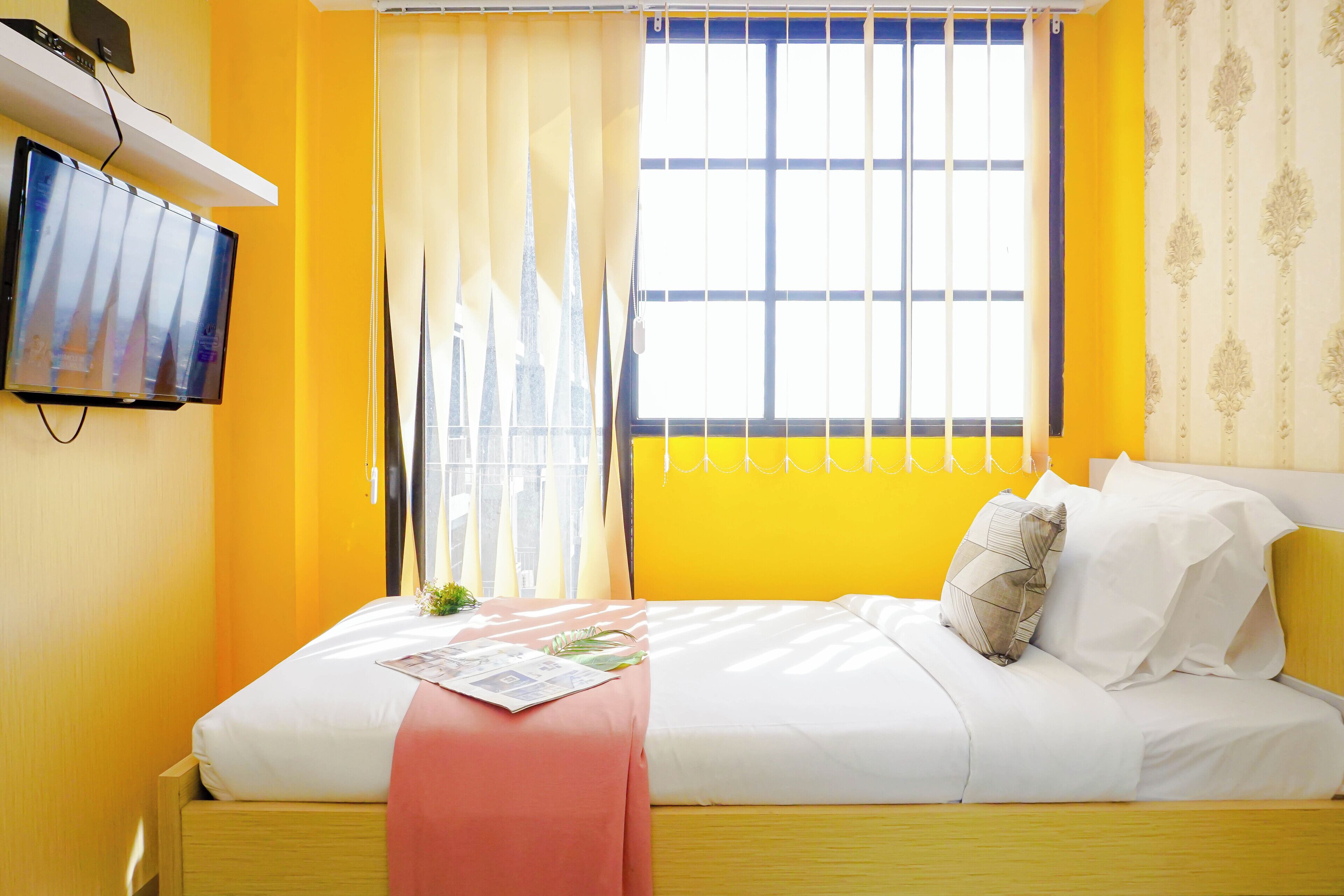 A room with a bed, a TV mounted on the wall, and a window with curtains.