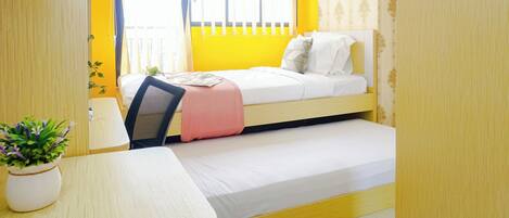 A compact room with a bed, a desk, and a potted plant.