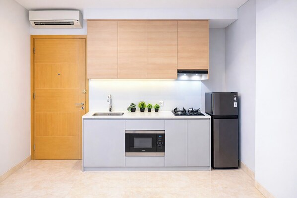 Una cocina compacta con puerta de madera, horno integrado, estufa a gas y refrigerador.