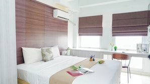 Een hotelkamer met een bed, nachtkastje, raam met zonwering en een airconditioning.