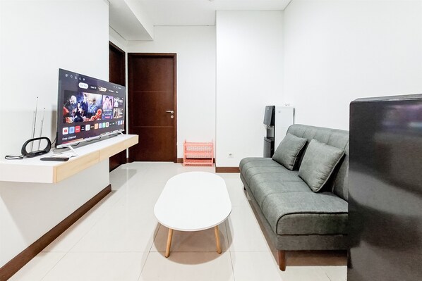 A modern living room with a flat-screen TV, a grey sofa, a white coffee table, and a small pink basket. - White Tone 2Br At Springwood Residence Tangerang (Tangerang)