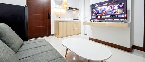 A modern living room with a grey sofa, a small white table, and a TV mounted on the wall displaying various channels.