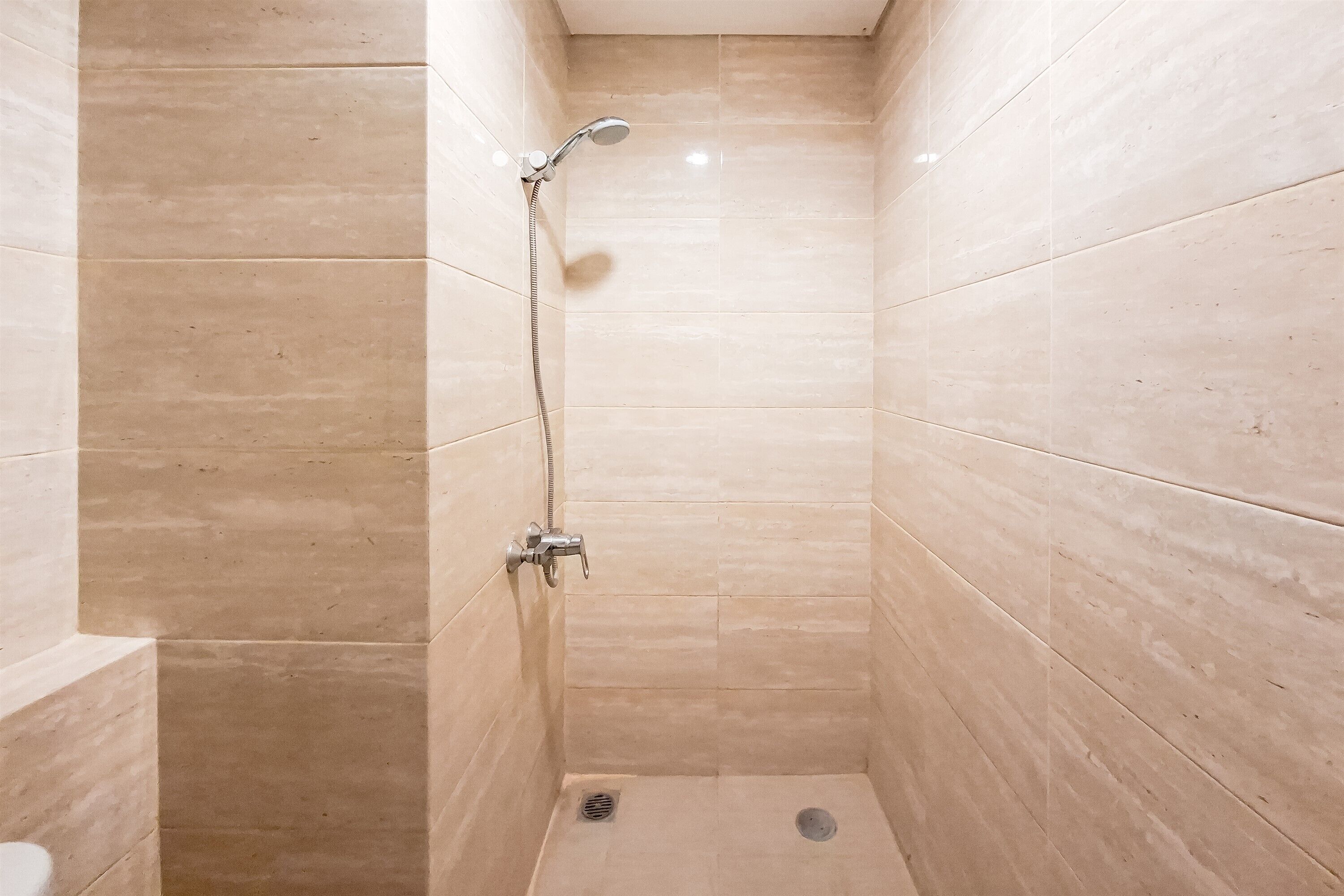 A small, tiled shower room with a handheld showerhead and a wall-mounted faucet.
