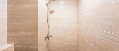 A small, tiled shower room with a handheld showerhead and a wall-mounted faucet.