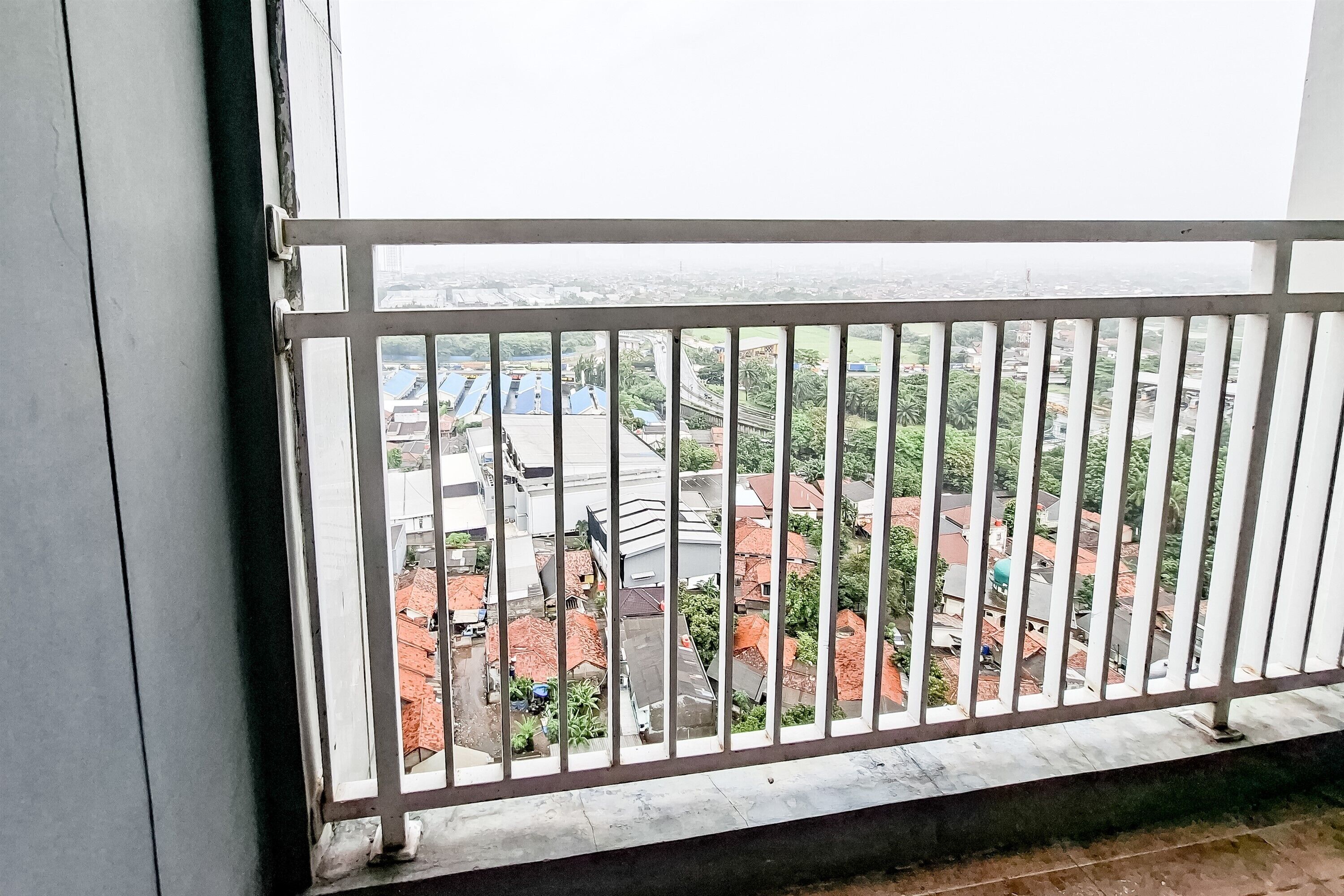 A balcony with a metal railing overlooking a residential area with houses and greenery.