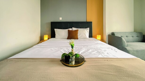 A neatly made bed with white linens, a dark headboard, and two bedside lamps. - Neat Studio At Daan Mogot City Apartment (Jakarta)