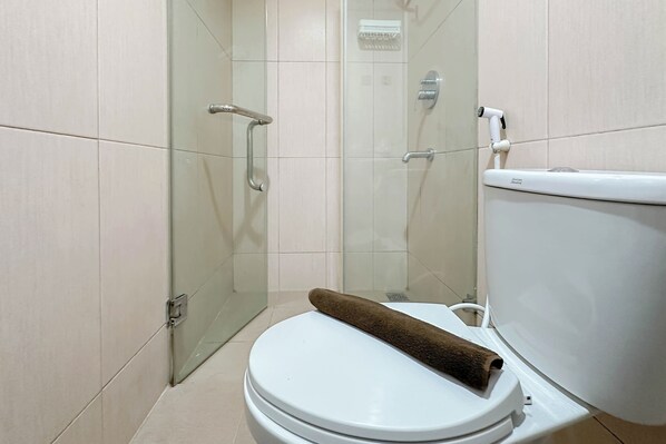 A bathroom with a glass-enclosed shower, a white toilet, and a towel on the toilet seat. - Strategic Location Studio At Tamansari Papilio Apartment (Surabaya)