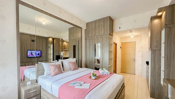 A modern bedroom with a large bed, a TV, a wardrobe, and a bathroom visible through an open door. - Cozy Living Studio Near Merr At Bale Hinggil Apartment (Surabaya)