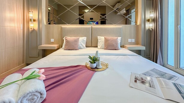 A hotel room with a large bed, a bedside table, a nightstand, a window with curtains, and a view of the interior. - Lavish Studio At Orchard Supermall Mansion Apartment (Surabaya)
