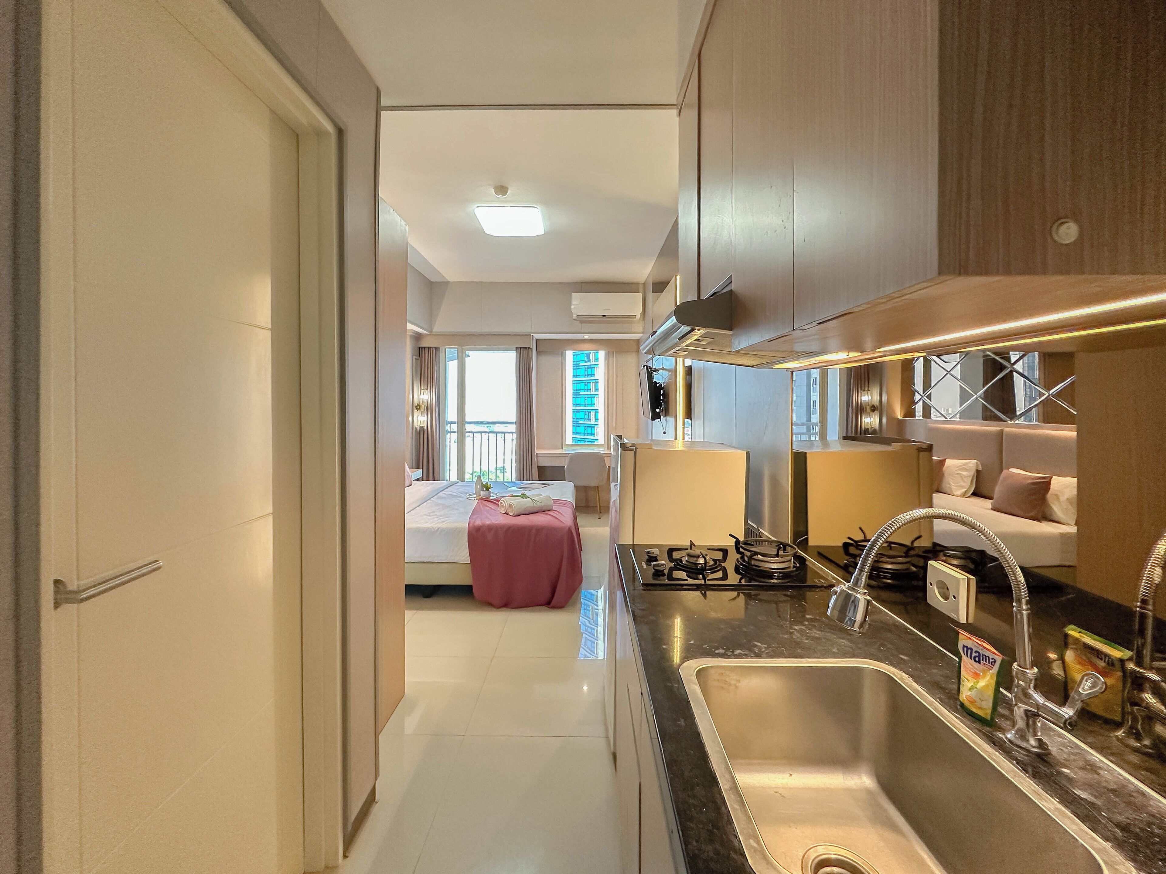 Una habitación de hotel moderna con cocina, una cama con edredón rosa y un balcón con vistas a la ciudad.