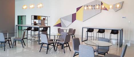Una sala de conferencias moderna con mesas y sillas de vidrio, arte geométrico en la pared e iluminación colgante.