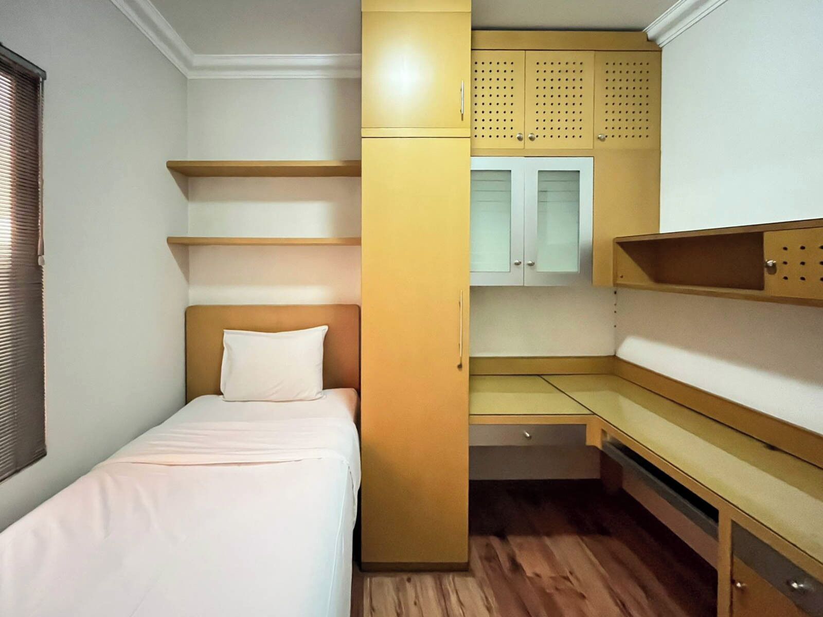 A compact room with a bed, built-in shelves, a wardrobe, and a small window.