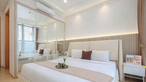 Una habitación de hotel moderna con una cama grande, una mesita de noche con un libro y un espejo amplio.
