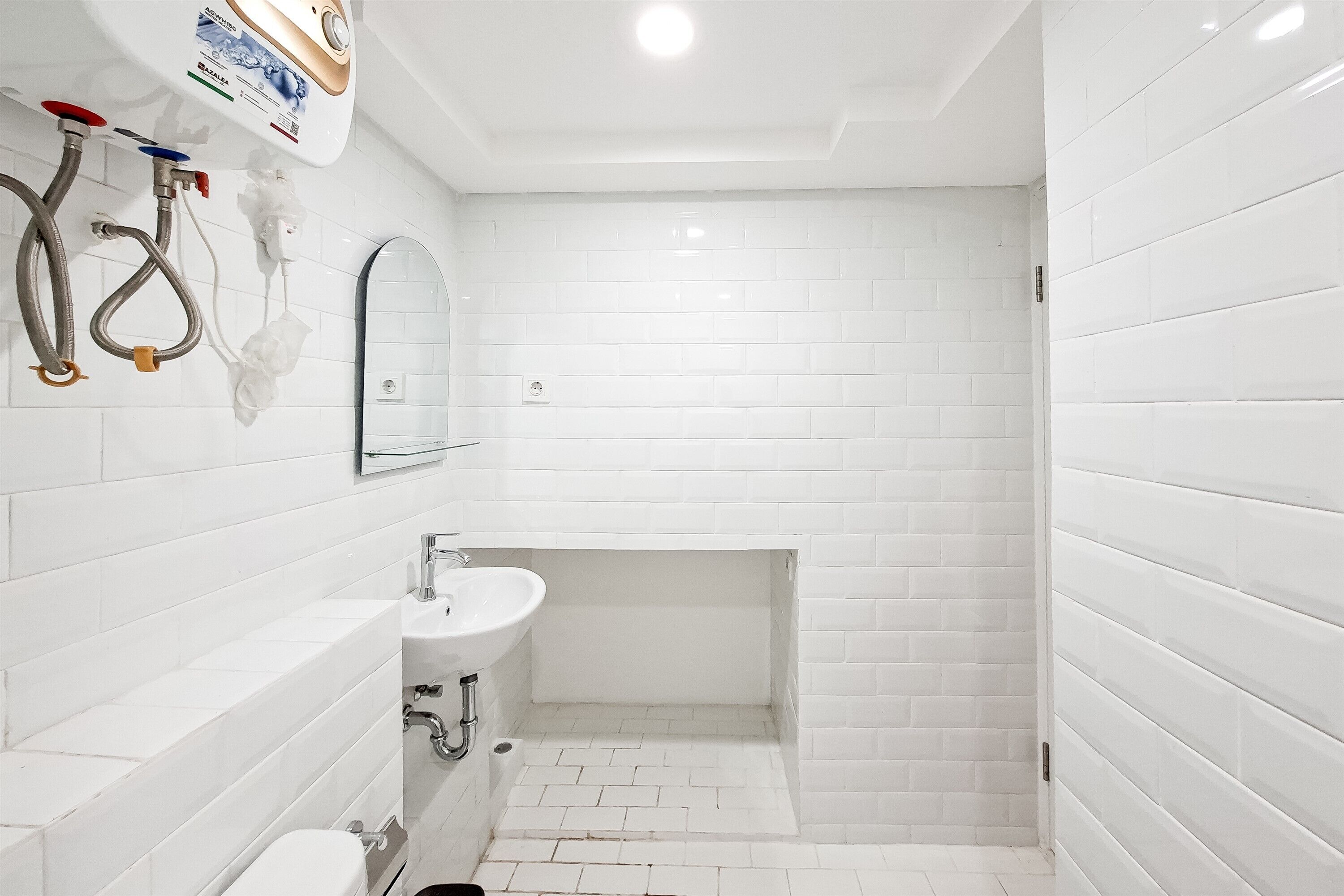 A bathroom with white tiled walls, a sink, and a shower area.