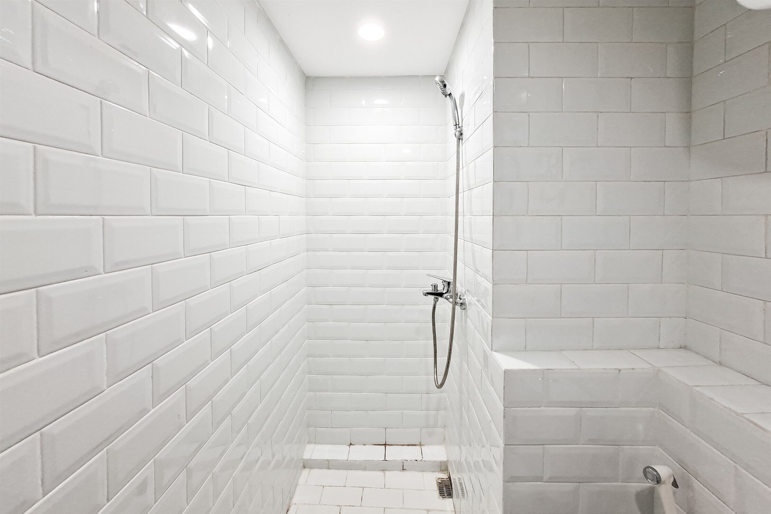 A bathroom with white subway tiles, a shower with a handheld showerhead, and a small bathtub.
