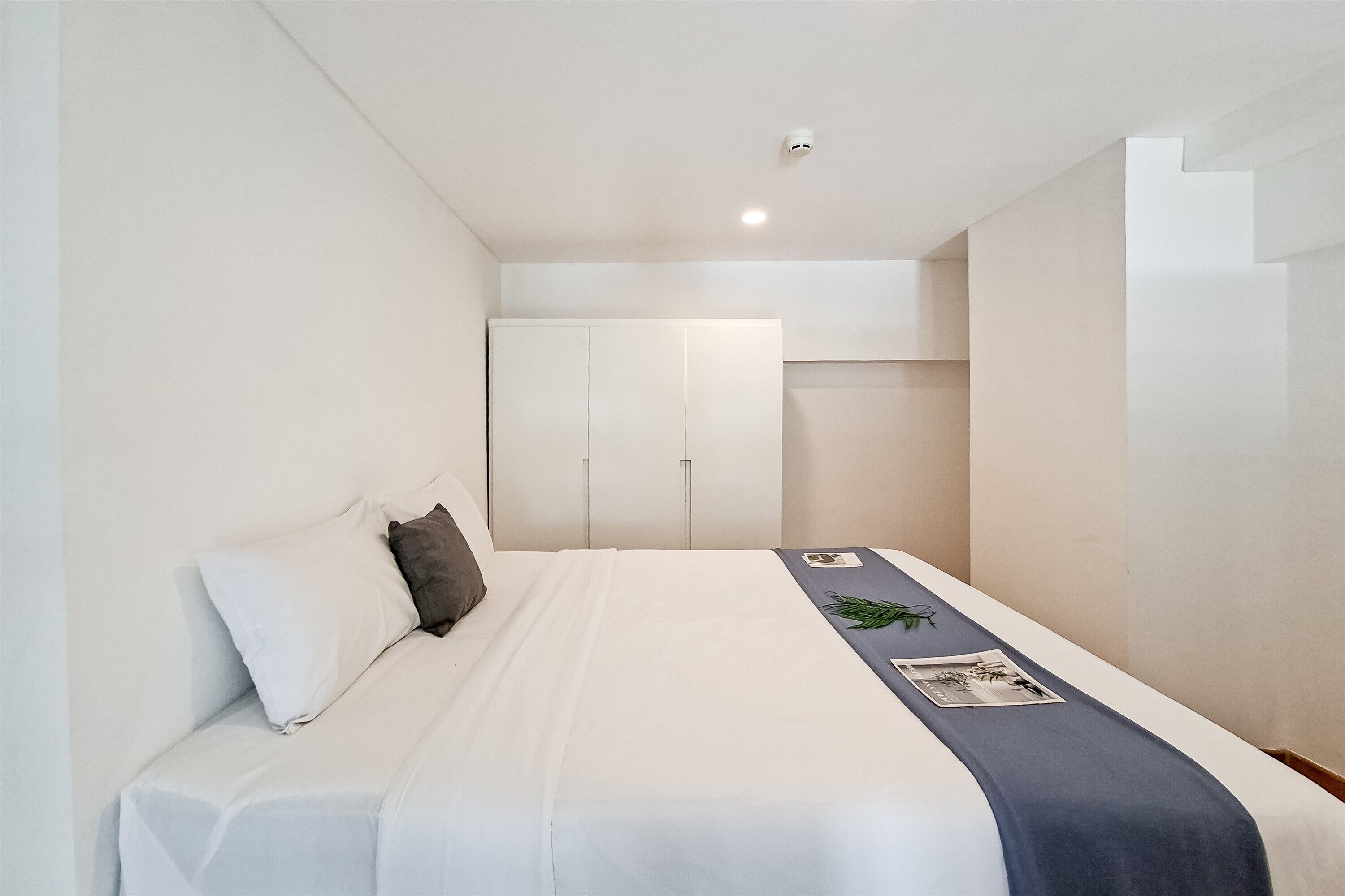 Ein Hotelzimmer mit Bett, weißen Wänden, einem Schrank und einem kleinen Tisch mit einer Zeitschrift.