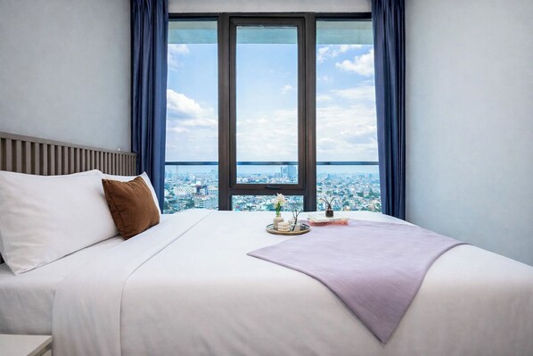 A hotel room with a large bed, a view of a cityscape through a window, and a city skyline visible through the window. - Chic And Lovely 2Br At Apartment Capitol Suites (Jakarta)