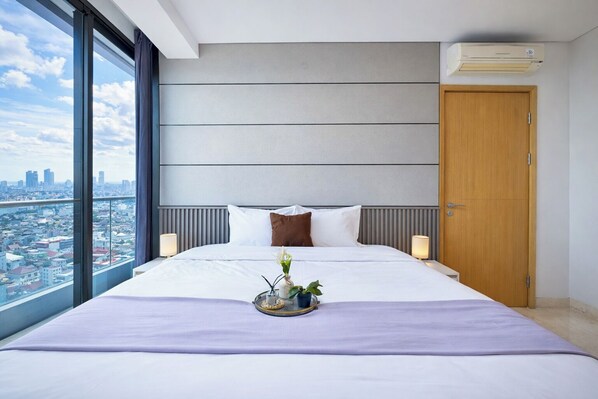 A modern hotel room with a large bed, a city view, and an air conditioning unit. - Comfy 2Br With City View At Capitol Suites Apartment (Jakarta)