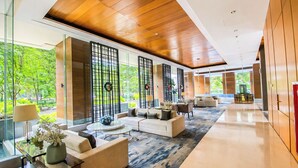 A spacious lobby with a modern design, featuring a large seating area with sofas and a coffee table, a glass partition with decorative screens, and a view of greenery outside. - Lavish Style 2Br At Capitol Suites Apartment (Jakarta)