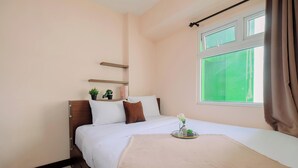 Une chambre d’hôtel avec un lit, une fenêtre avec des rideaux, une table de chevet avec une plante et une étagère au-dessus du lit.