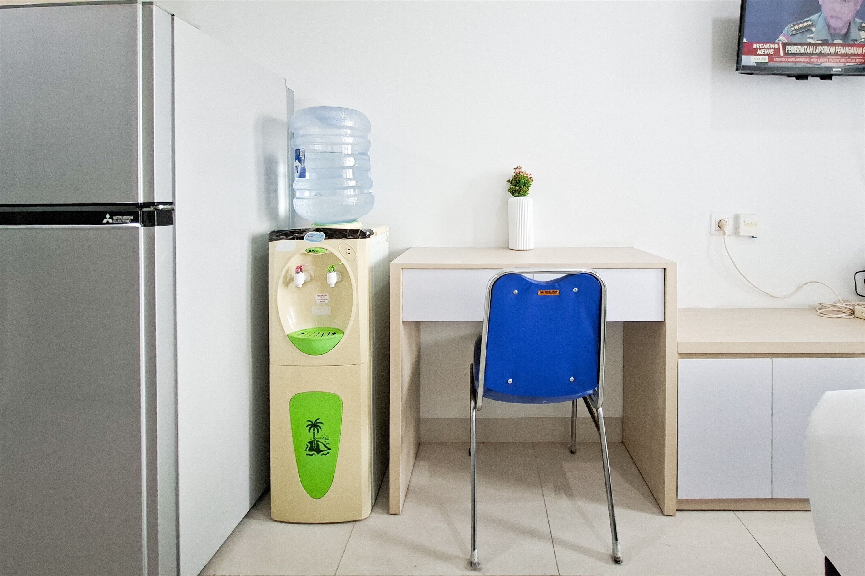 A compact kitchen with a refrigerator, a water dispenser, a desk, and a chair.