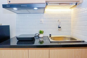 Une cuisine moderne avec un plan de travail noir, un évier en acier inoxydable, une hotte intégrée et une petite plante en pot.