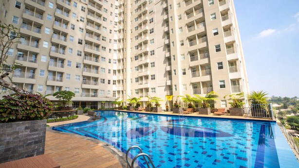 A high-rise residential building with a swimming pool and outdoor seating area. - Simply Studio Apartment Near Unpar At Parahyangan Residence (Bandung)