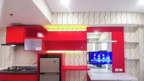 A modern kitchen with red cabinetry, a built-in stove, a refrigerator, and a wall-mounted TV. - Simply Studio Apartment Near Unpar At Parahyangan Residence (Bandung)