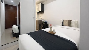 A hotel room with a bed, a small desk, a wardrobe, and a bathroom visible through an open door. - Basic Look Studio Apartment At Vittoria Residence (Jakarta)