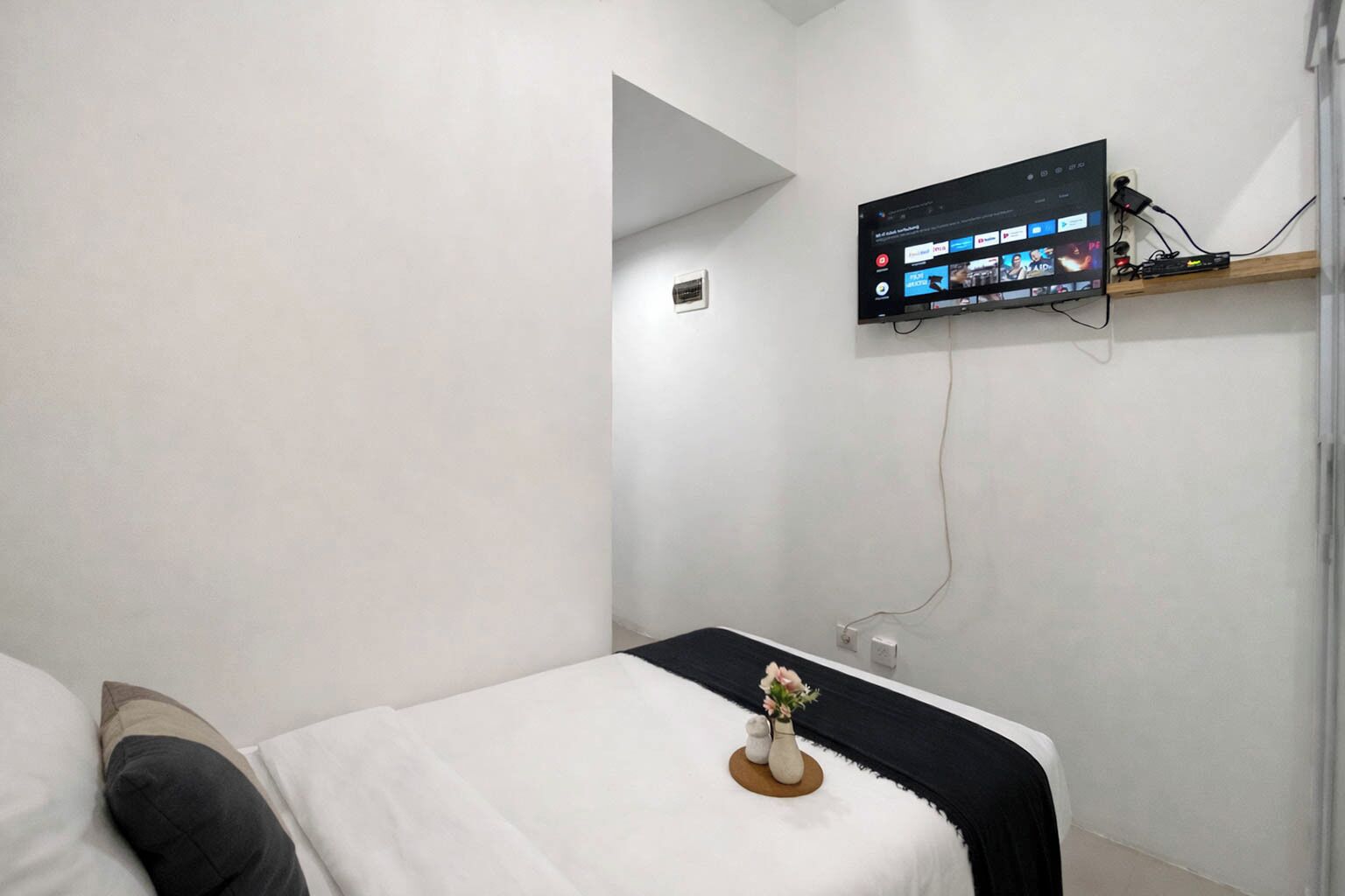 A modern hotel room with a bed, a mounted TV, and a small shelf.