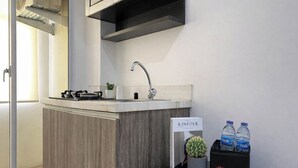 A modern kitchen with a built-in sink, a small stove, and a potted plant. There are two bottles of water and a box labeled "travello" on a black table. - Basic Look Studio Apartment At Vittoria Residence (Jakarta)