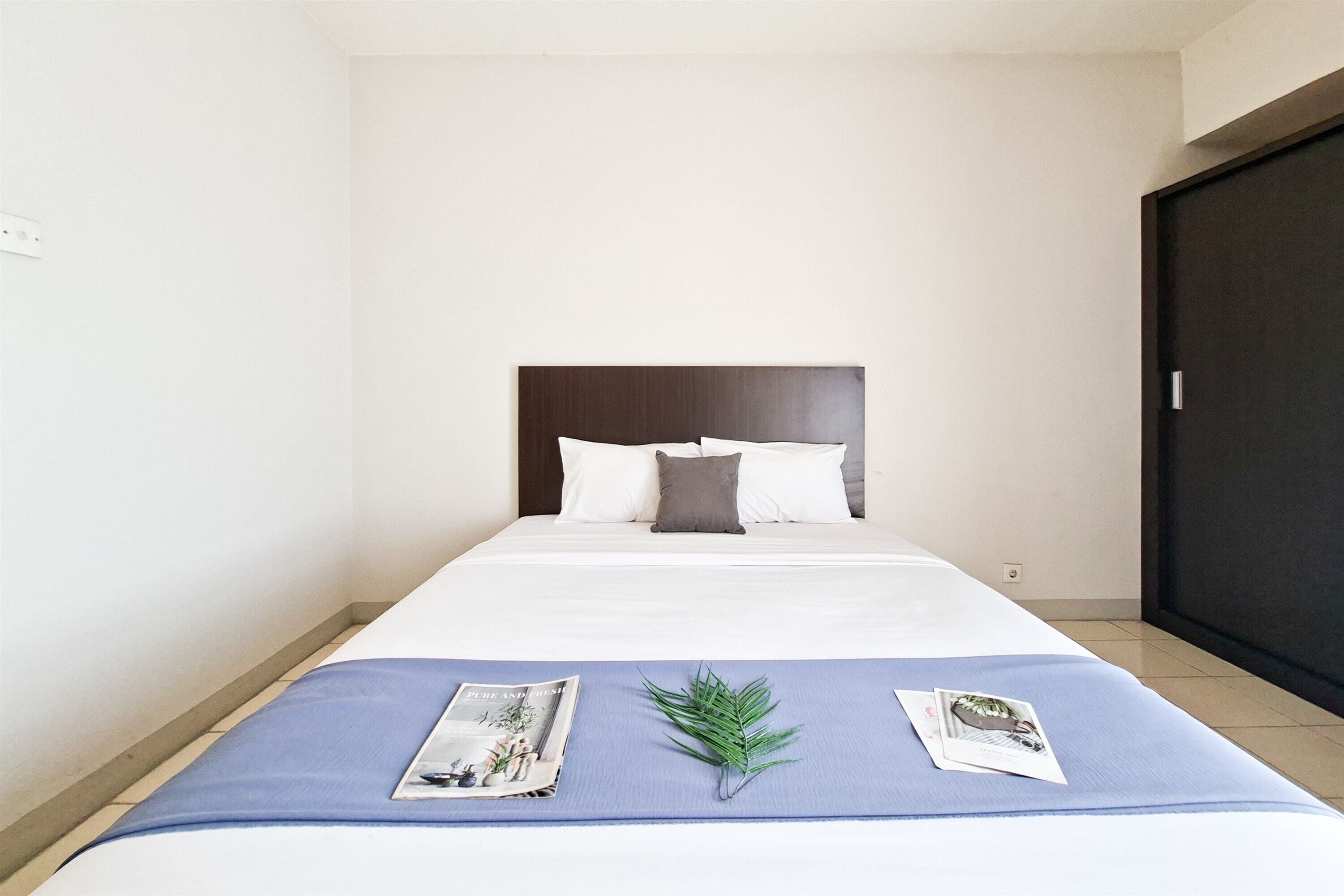 A neatly made bed with a dark headboard, white bedding, and a blue bedspread.