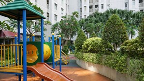 Ein Spielplatz mit Rutschen und Klettergerüsten, umgeben von üppigem Grün und einem Gebäude im Hintergrund.