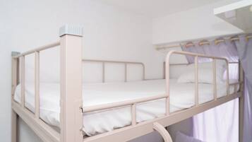 Una cama litera con escritorio extraíble, ropa de cama blanca y una cortina.