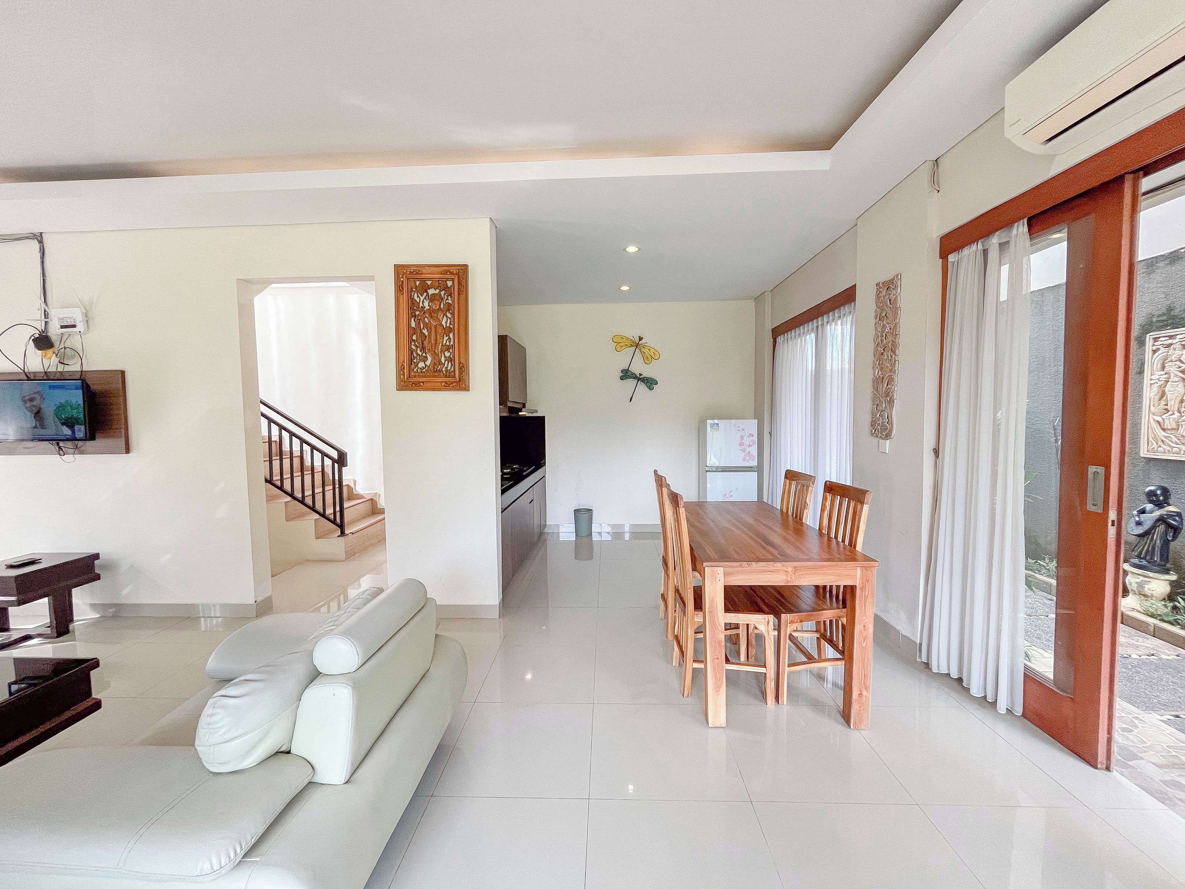 Uma sala de estar moderna com sofá, mesa de jantar e cadeiras. Há uma escada que leva a outro nível, uma área de cozinha e um espaço de refeições com vista para o exterior.